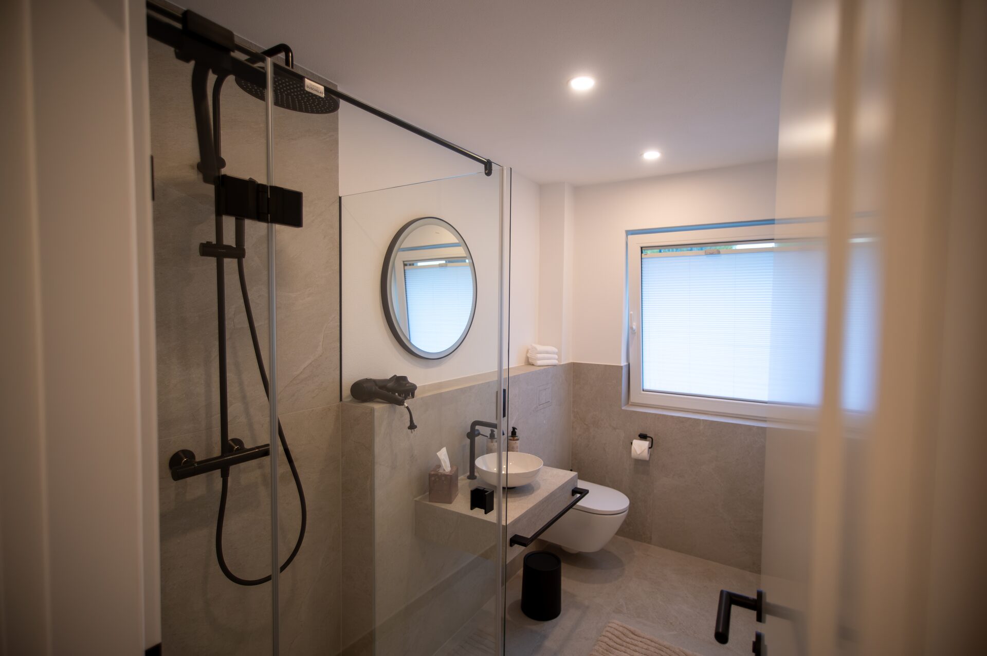 Bad mit Regendusche hinter Glas, rundem Spiegel und Aufsatzwaschbecken