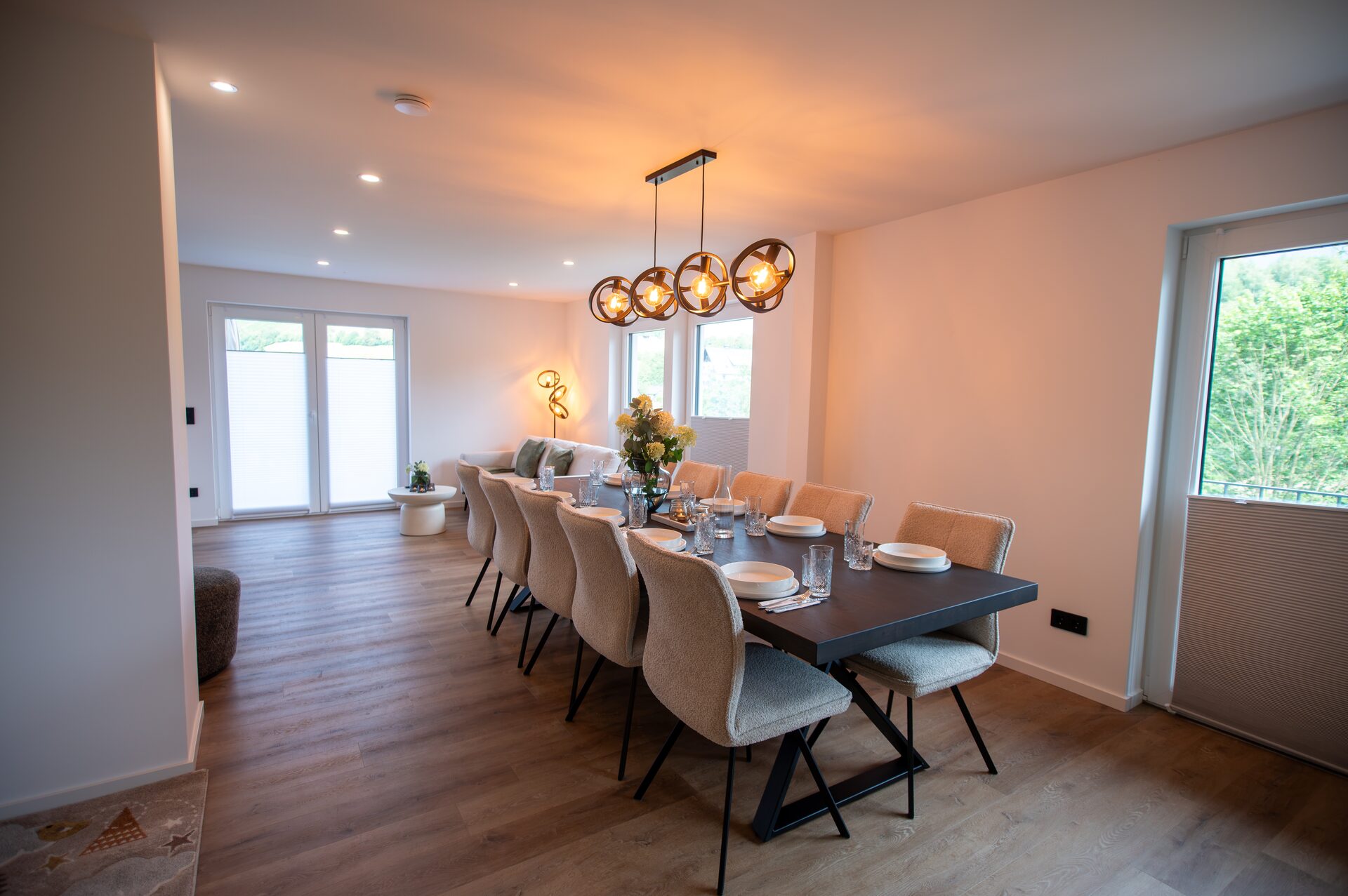 Lange Tafel unter Ringleuchten, dahinter der offene Wohnbereich