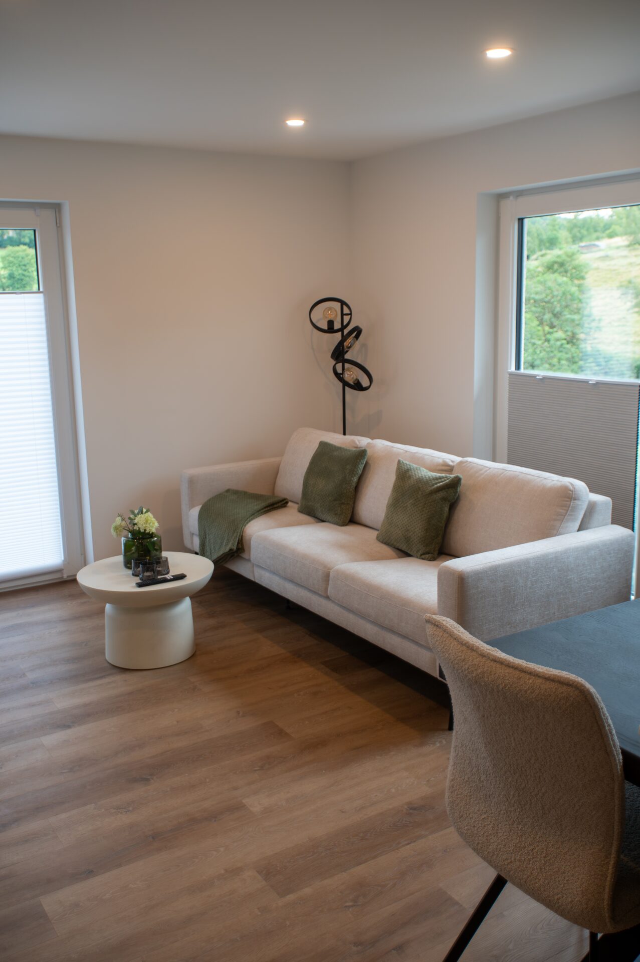 Helles Sofa mit grünen Kissen am Fenster, davor ein runder Beistelltisch